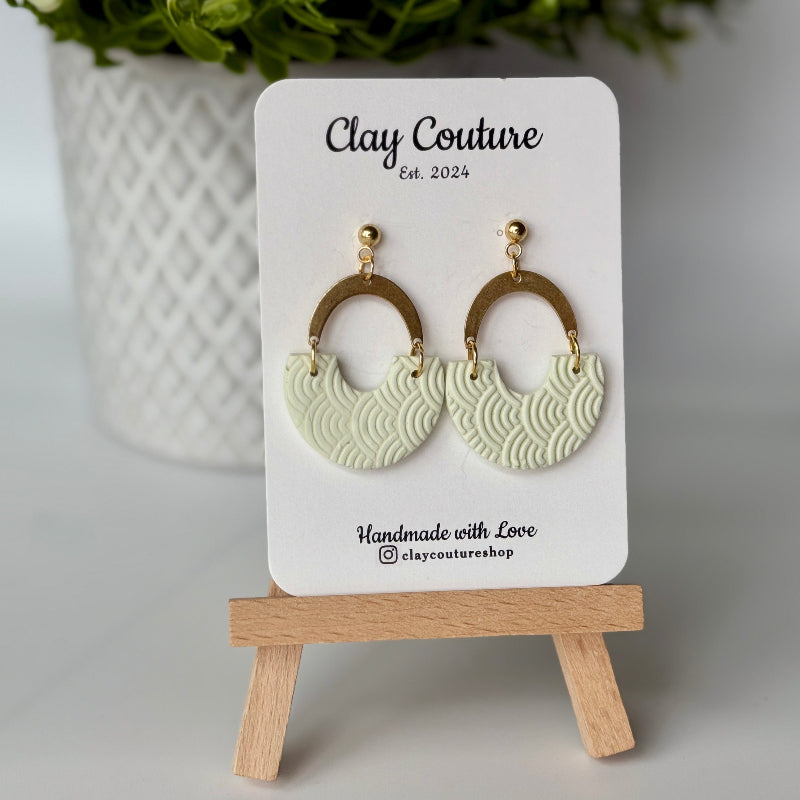 Polymer clay earrings in Sage Mist color with brass connectors and 18K gold plated studs  on a 'Clay Couture' branded card with a wooden stand