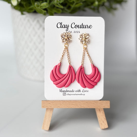 Pink clay earrings on a 'Clay Couture' branded card with a wooden stand.
