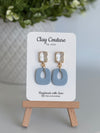 Dusty Blue polymer clay earrings with a crystal stud on a 'Clay Couture' branded card with a wooden stand.