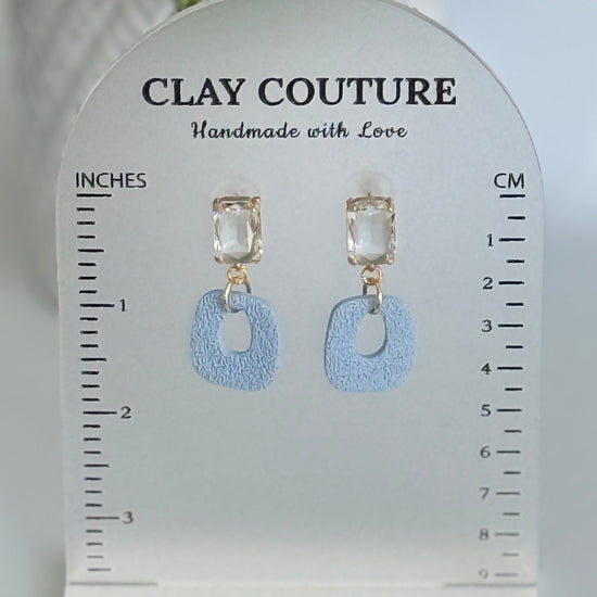 Dusty Blue polymer clay earrings with a crystal stud on a 'Clay Couture' branded size stand