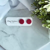 Red textured earrings on a Clay Couture card with greenery in the background