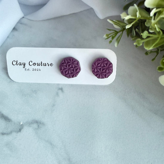 Purple geometric earrings on a Clay Couture branded card with a marble background