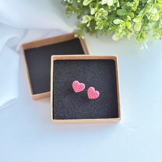 Pink heart-shaped earrings in a jewelry box with greenery in the background