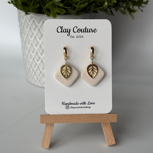 Polymer clay  earriings in Irish Creme color with and gold huggies brass charms on a 'Clay Couture' branded card with a plant in the background.