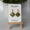 Polymer clay  earrings in Olive Grove color with and gold huggies brass charms on a 'Clay Couture' branded card with a plant in the background.