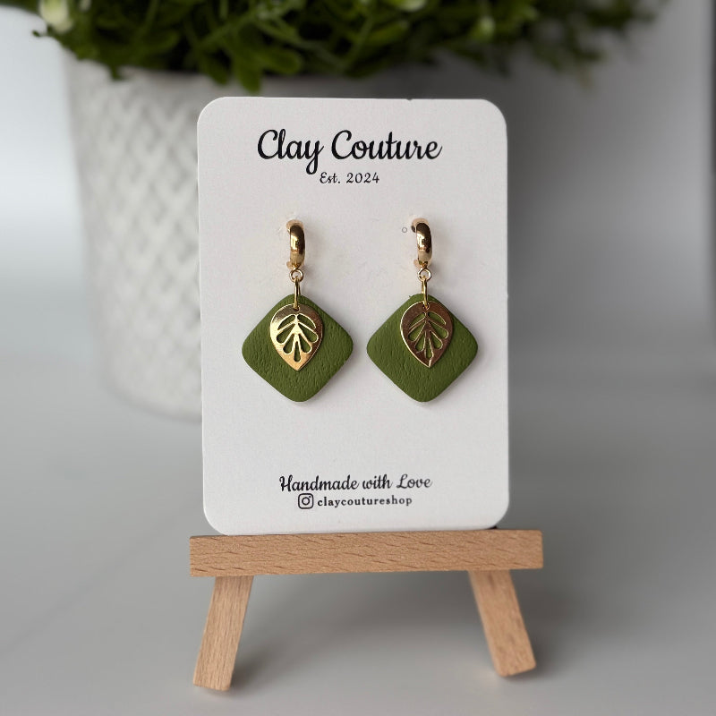 Polymer clay  earrings in Olive Grove color with and gold huggies brass charms on a 'Clay Couture' branded card with a plant in the background.
