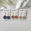 Three pairs of clay flower earrings on 'Clay Couture' cards with a white background.