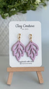 Embossed leaf design  earrings in Mauve color with gold plated hoops on a 'Clay Couture' branded card with a plant in the background.
