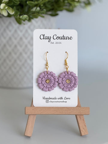 Mauve flower earrings on a Clay Couture branded card with a wooden stand.