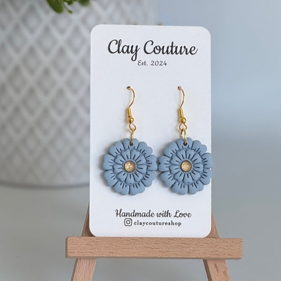 Dusty Blue flower earrings on a Clay Couture branded card with a wooden stand.