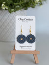 Slate Blue flower earrings on a Clay Couture branded card with a wooden stand.