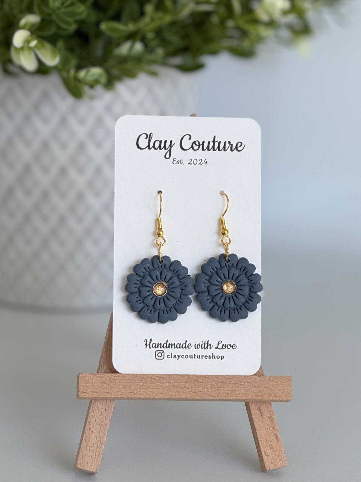 Slate Blue flower earrings on a Clay Couture branded card with a wooden stand.