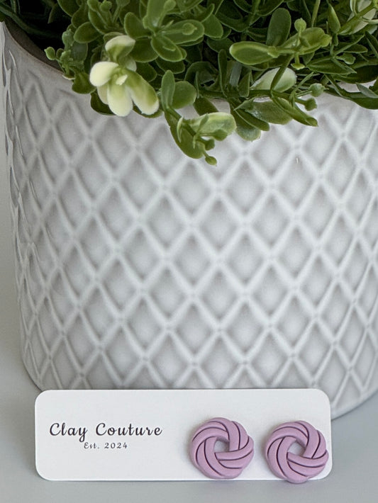 Mauve Polymer Clay knot earrings on a Clay Couture card with a potted plant in the background.
