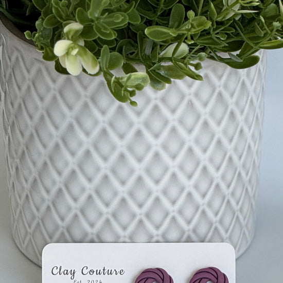 Plum Polymer Clay knot earrings on a Clay Couture card with a potted plant in the background