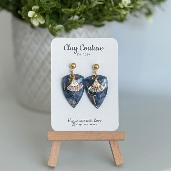 Sapphire Blue dagger shaped polymer clay  earrings  with a resin finish and gold accents on a Clay Couture branded card.